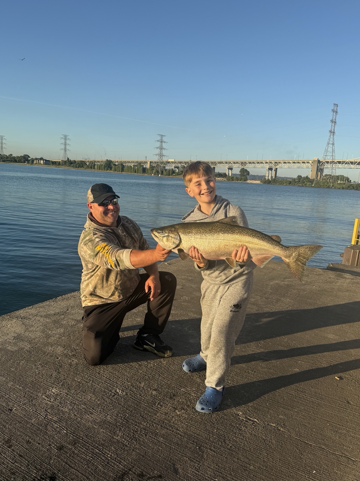 Two anglers holding a large fish beside open water
